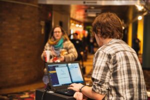 indoors, movie theatre, ticket, ticket check-in, customer, lobby, theatre, movie, computer, scanner, brown computer, brown laptop, brown movie, brown theater, brown check, ticket, lobby, lobby, scanner, scanner, scanner, scanner, scanner