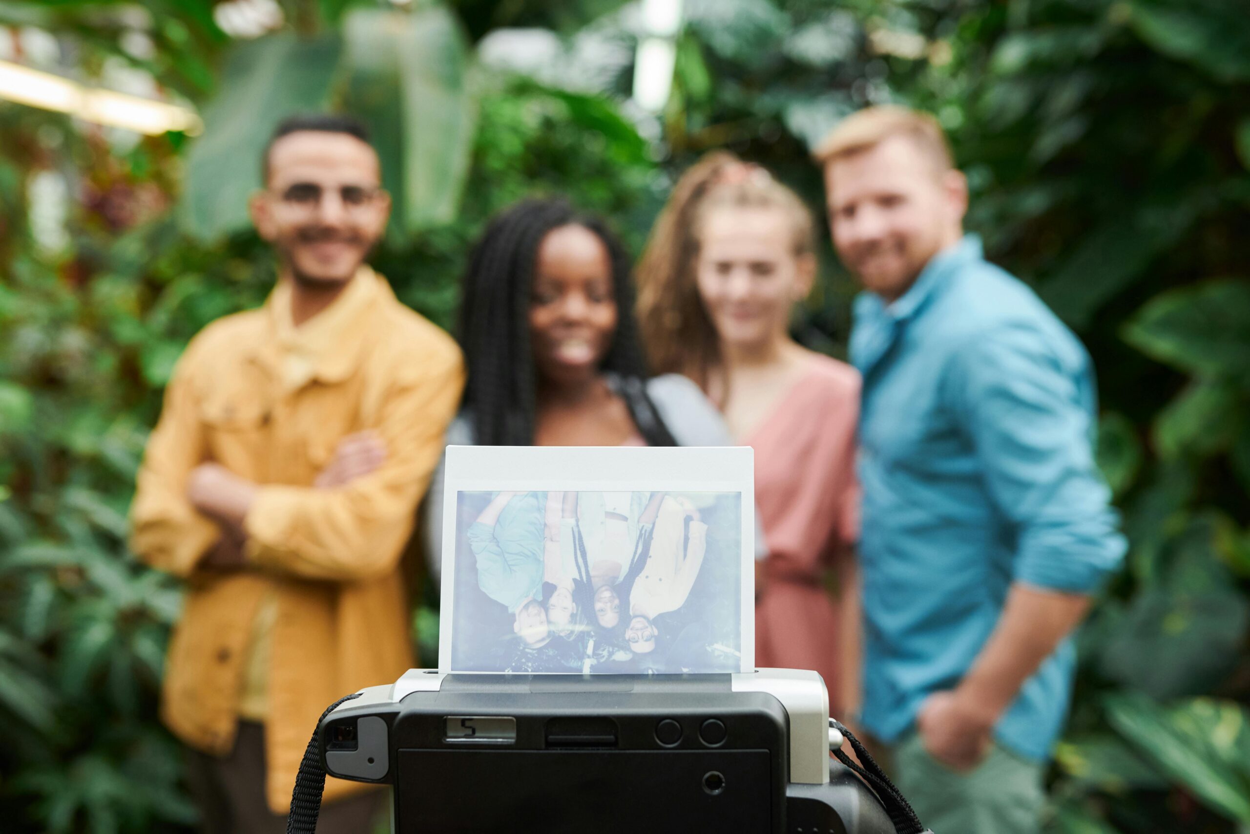 Group of friends posing for a photo with a vintage camera amidst lush greenery, smiling and happy.