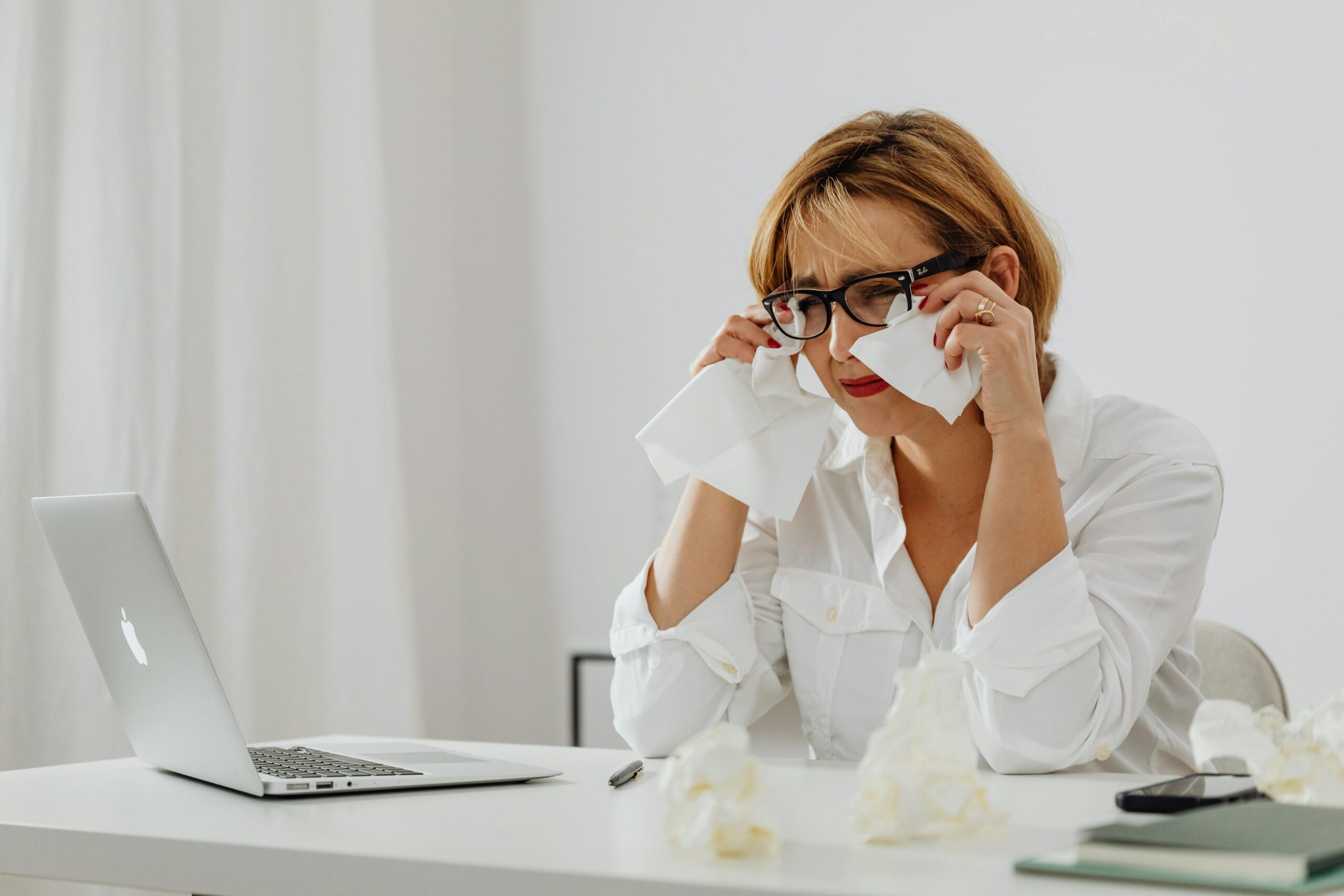Woman experiencing stress at work using a laptop with tissues on a desk.