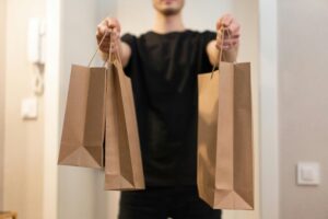 Adult holding several paper bags representing delivery service indoors.