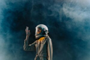 A modern astronaut in a spacesuit raises their hand amidst ethereal smoke, blue tones.