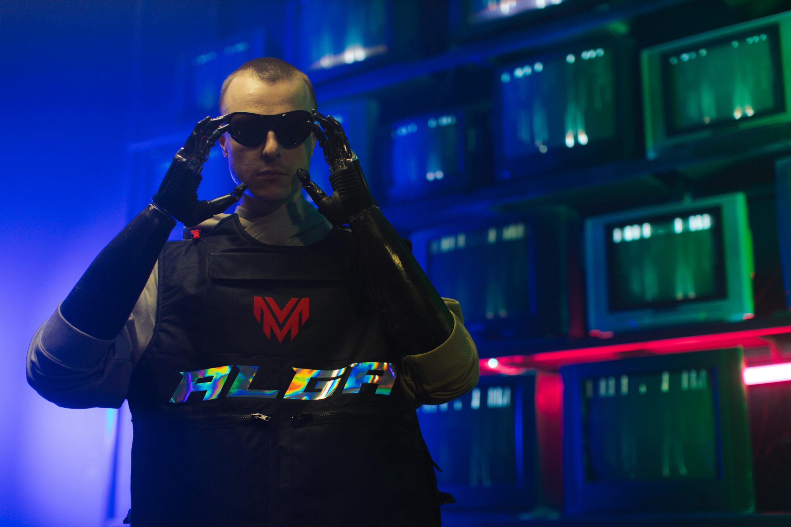 Man in cybernetic outfit adjusts sunglasses, neon-lit room with retro aesthetic.