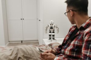 A man examines a robotic toy placed on a table in a contemporary bedroom setting.