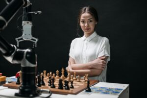 A young woman in a white blouse playing chess against a robot arm.