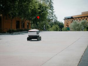 A futuristic autonomous delivery robot moving on an empty city street.