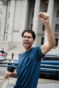 A man passionately protests with a raised fist in front of a government building, embodying activism.